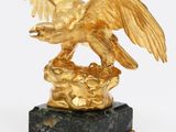 une image représentant une statue d'aigle en or posée sur un socle en marbre noir