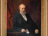 portrait d'un homme en costume noir et chemise blanche, assis sur une chaise