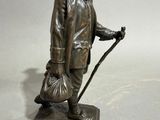 statue en bronze représentant un homme muni d'une canne et d'un chapeau, tenant un sac
