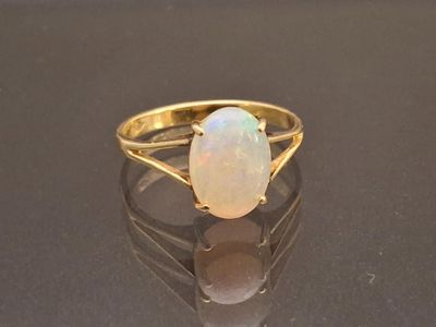 yellow gold ring with a white opal stone on a black surface