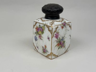 une petite boîte blanche avec un couvercle noir orné de fleurs