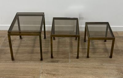 trois tables d'appoint en verre et en laiton posées sur un parquet