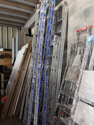 Plusieurs échelles sont empilées contre un mur dans un entrepôt.