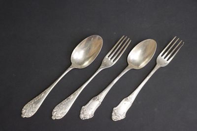 quatre cuillères en argent et une fourchette posées sur un fond noir