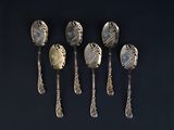 six silver spoons are lined up on a black surface