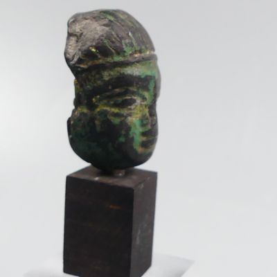 sculpture représentant une tête, posée sur un socle en bois, sur une surface blanche