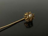 a close up of a gold brooch with a pearl in the center