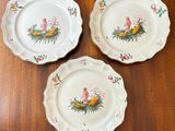 three white plates with birds and flowers on them sitting on a wooden table