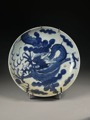 blue and white plate with a dragon on it on a stand