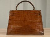 crocodile skin handbag on a wooden table with a curtain in the background