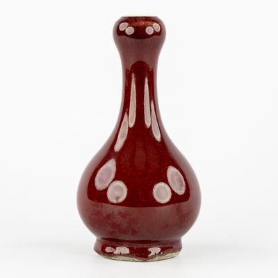 un vase rouge posé sur une surface blanche