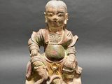 an old statue of a man sitting on a rock holding a ball