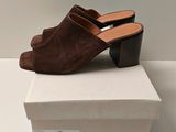 a pair of brown sued mules on top of a white box