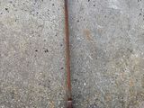 a rusted metal pole on the ground next to a brick wall