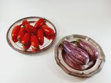 tomatoes and eggplant on a plate next to a bowl of eggplant