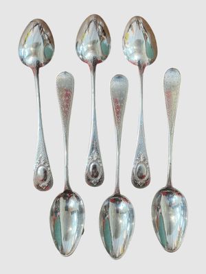 six cuillères en argent sont alignées sur une surface blanche