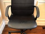 black leather office chair with armrests and casteors on hardwood floor