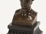 un buste antique en bronze représentant un homme aux cheveux bouclés, posé sur un socle