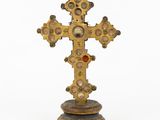 une vieille croix en or posée sur un socle en bois, avec une pierre rouge au centre