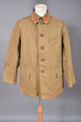 une veste beige à boutons rouges posée sur un présentoir pour mannequin