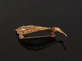 an image of a gold feather broochle on a black surface