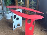 a red surfboard on a stand next to a potted plant