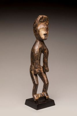 une statue en bois représentant un homme debout sur un socle noir