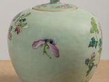 a green vase with flowers painted on it on a table