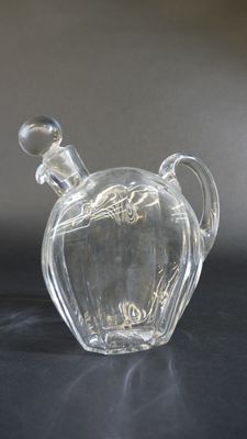 bouteille en verre transparent avec une anse, posée sur un support noir