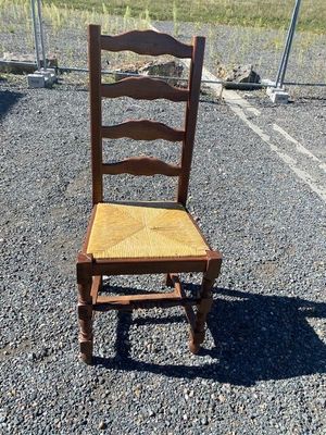 an old wooden chair sitting in a parking lot next to a chain link fence