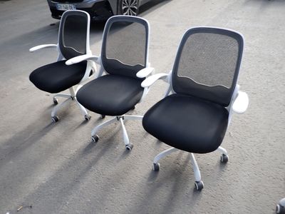 three office chairs sitting in a parking lot with a car in the background