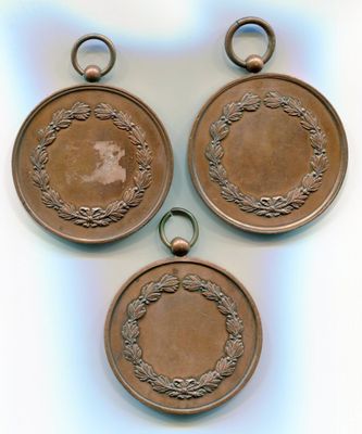 Trois médailles anciennes en bronze sont exposées sur un fond blanc