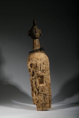 une vieille statue en bois représentant une personne assise sur un rocher, avec un oiseau perché dessus