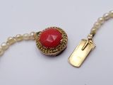 pearl necklace with a red stone and a gold clasp on a white background
