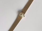 une image représentant une montre en or avec un cadran blanc posée sur une surface blanche
