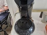 a coffee maker sitting on a table with a person in a wheel chair in the background