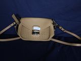 sac à main en cuir beige orné de boucles métalliques sur fond bleu