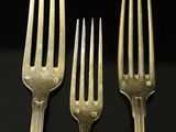 three forks are sitting next to each other on a black surface