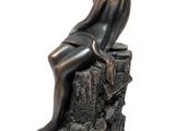 bronze statue of a woman sitting on a rock with her legs crossed