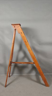 Un vieux chevalet en bois est adossé à un mur gris.