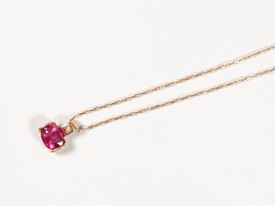 un gros plan d'un collier avec une pierre rose sur une chaîne en or