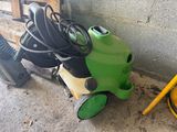 un aspirateur vert et noir et un tuyau jaune posé par terre
