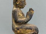 statue of a person sitting on a block with their hands clasped