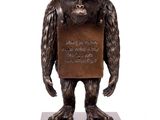 statue en bronze représentant un gorille tenant une pancarte, posée sur un socle en marbre