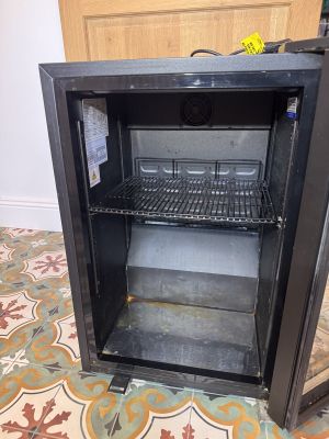 a small black refrigerator with a door open on a tiled floor