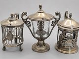 two silverplated teapots and a birdcage with a bird on top
