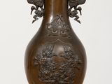 un vase en bronze posé sur un socle en bois, lui-même posé sur une table