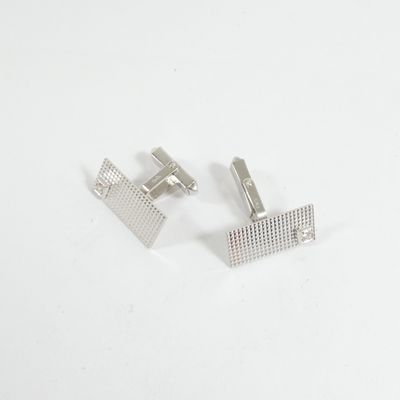 une paire de boutons de manchette en argent sur une surface blanche, sur fond blanc