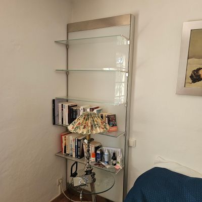 une étagère en verre avec des livres et une lampe dans un coin