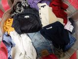a basket full of clothes on a bed with a red blanket